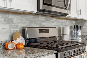 Une cuisine équipée d’une hotte en acier inoxydable, d’un four à micro-ondes installé au-dessus, d’un plan de travail en granit et d’un ensemble de couteaux accrochés au mur.