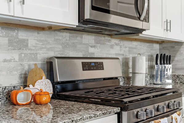 Una cocina con una campana extractora de acero inoxidable, un microondas encima, una encimera de granito y un juego de cuchillos en la pared.