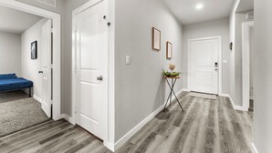 A hallway with a bed, a door, a small table with a plant, and a framed picture on the wall. - Premium  4BR Home Near Midland airport (Odessa)
