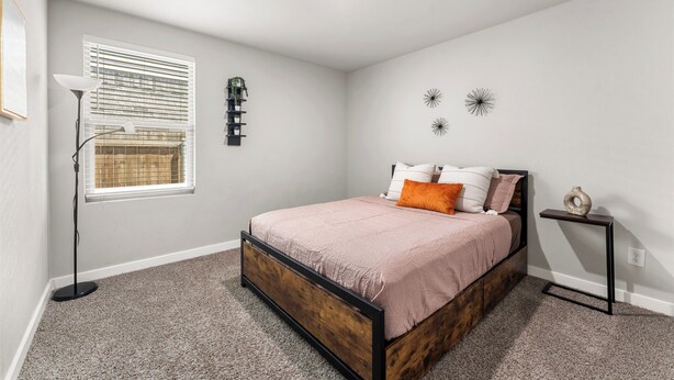 A bedroom with a bed, a bedside table, a floor lamp, a window with blinds, and wall decorations. - Premium  4BR Home Near Midland airport (Odessa)