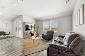 A spacious living area with a sofa, a dining table with chairs, a television, and a fireplace.