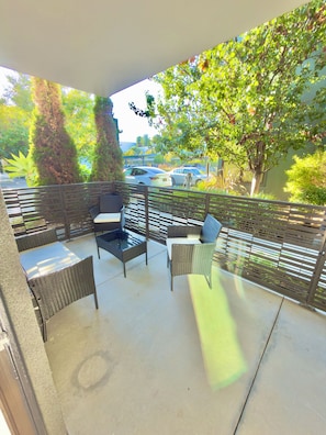 An outdoor patio with wicker furniture and a view of parked cars and greenery. - Modern, 1-bedroom, near Stanford and Meta, with parking. (Menlo Park)