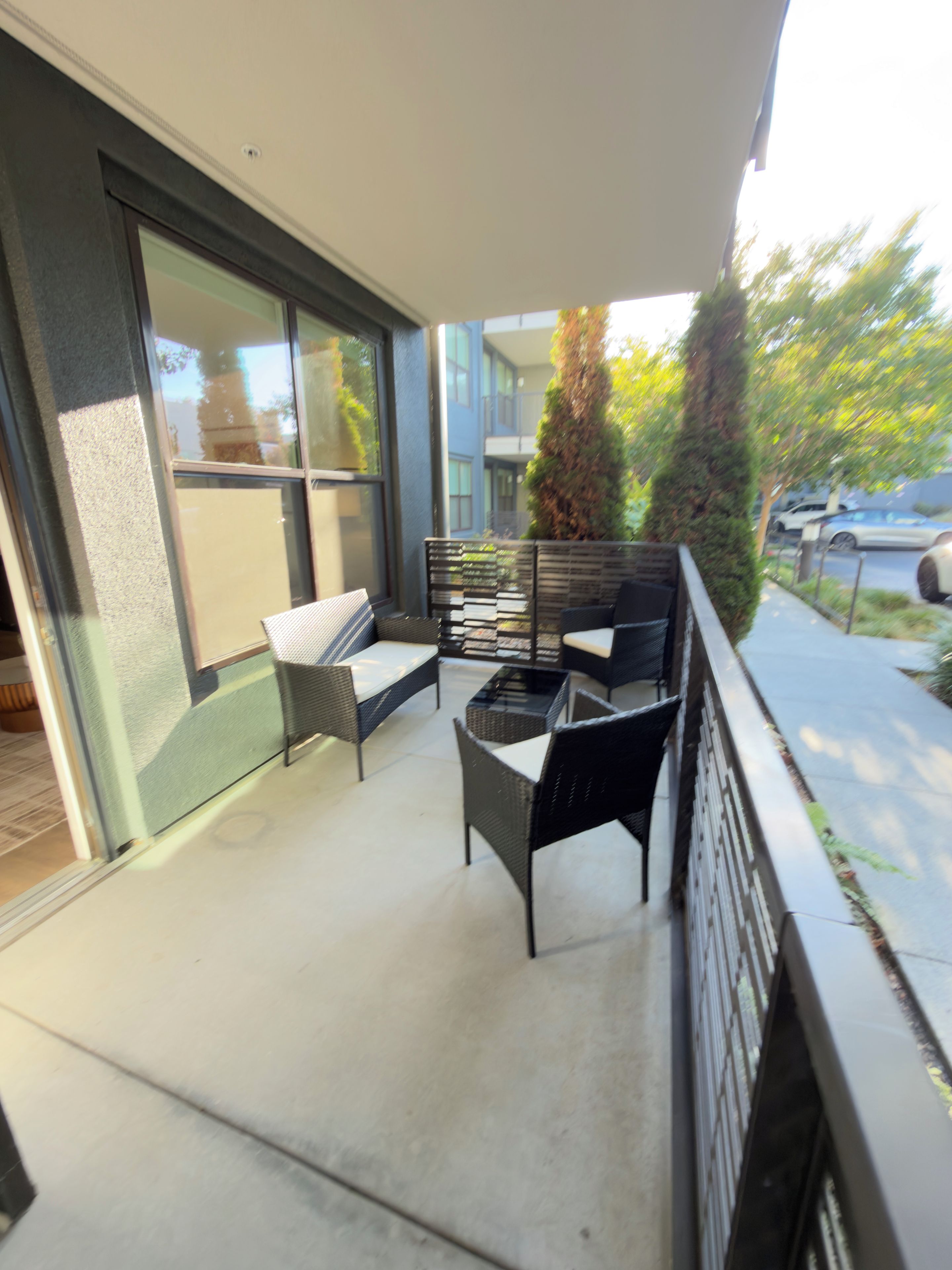 A balcony with outdoor furniture, a glass door, and a view of a building and parked cars.