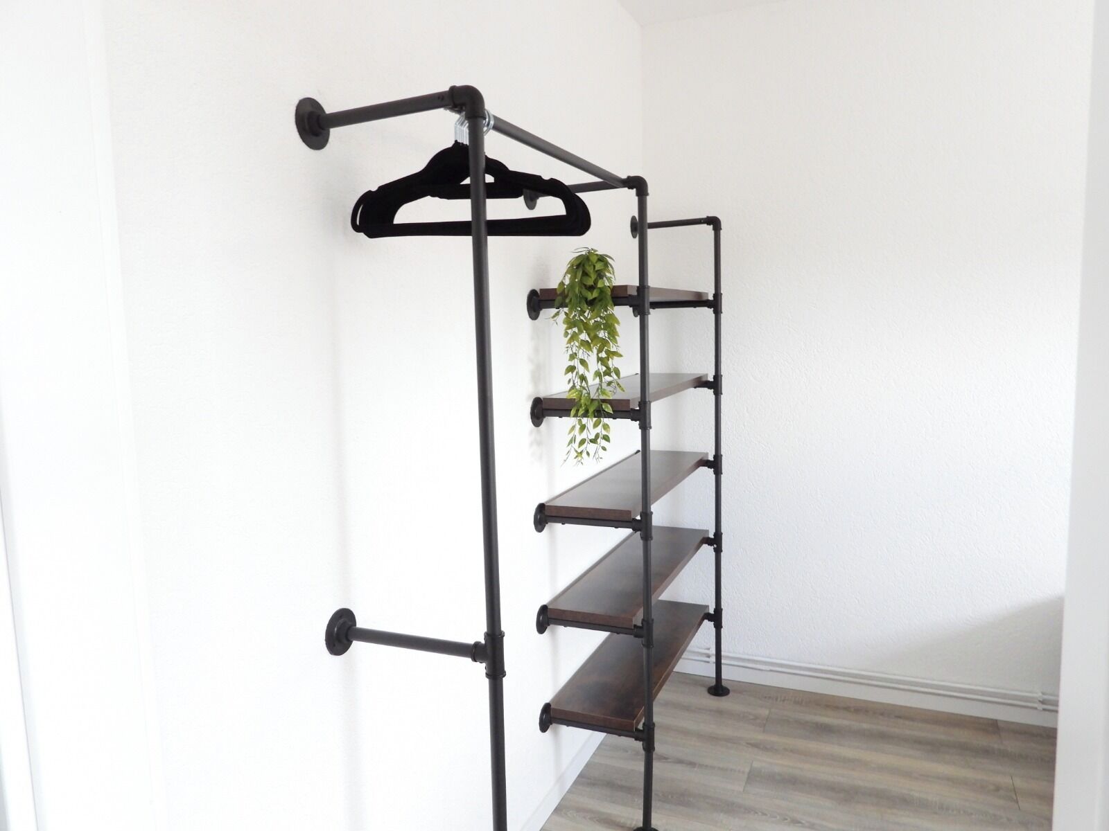 Ein schwarzes, an der Wand befestigtes Regal aus Metall mit mehreren Ablageflächen und einer hängenden Pflanze.