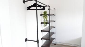 Ein schwarzes, an der Wand befestigtes Regal aus Metall mit mehreren Ablageflächen und einer hängenden Pflanze.