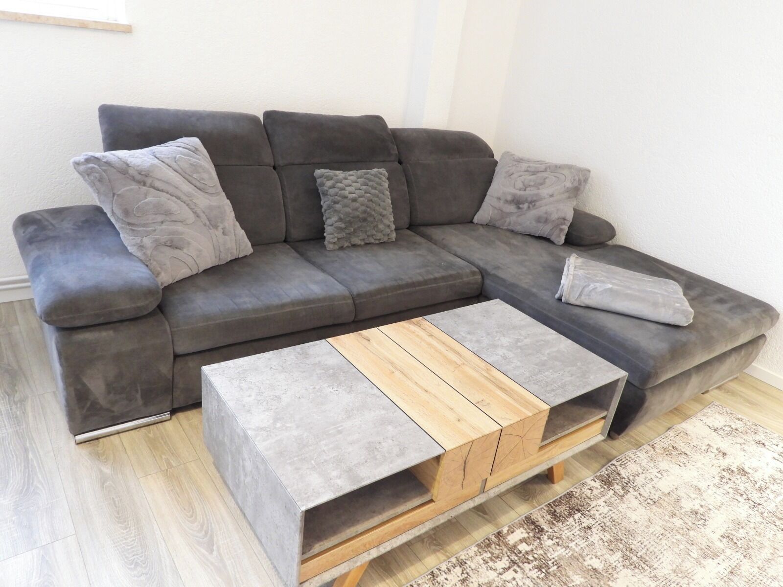 Ein graues Ecksofa mit einem Holztisch davor.
