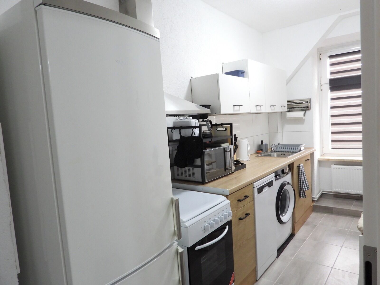 Une cuisine compacte équipée d’un réfrigérateur, d’un four à micro-ondes, d’un four et d’un lave-linge.