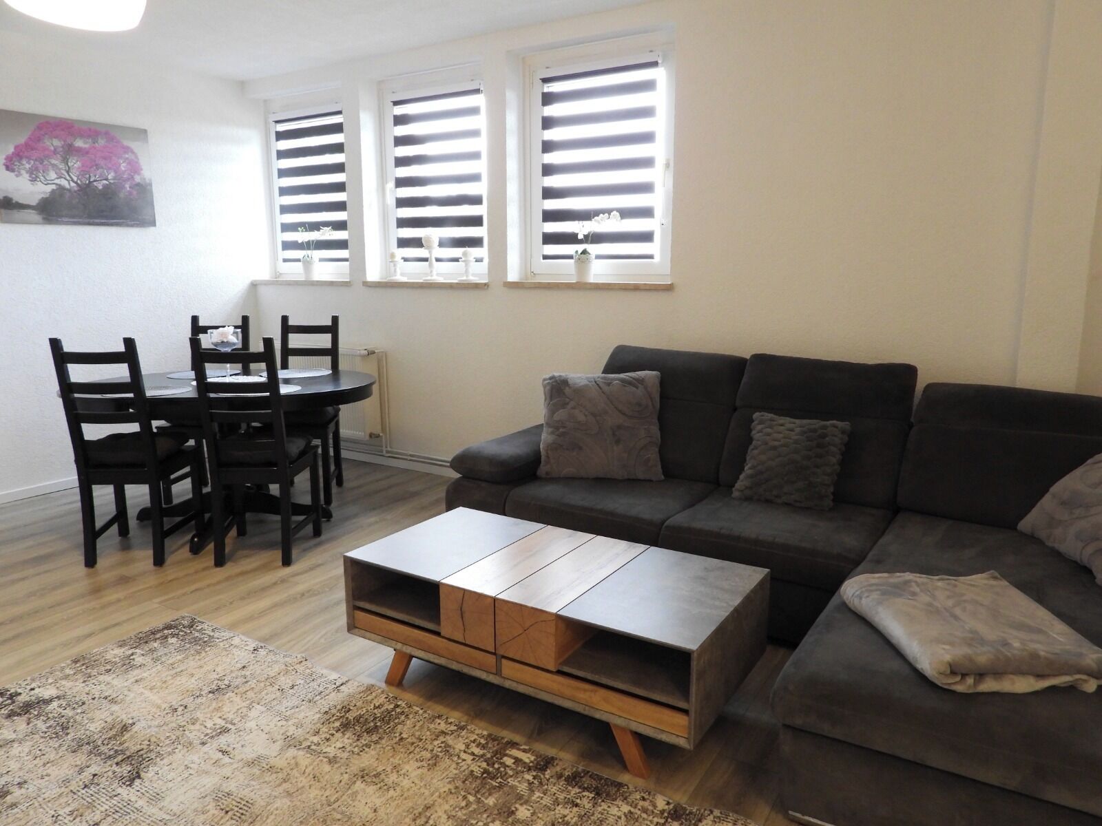 Ein Wohnzimmer mit einem dunkelgrauen Sofa, einem Holztisch und einem Essbereich mit Tisch und Stühlen.