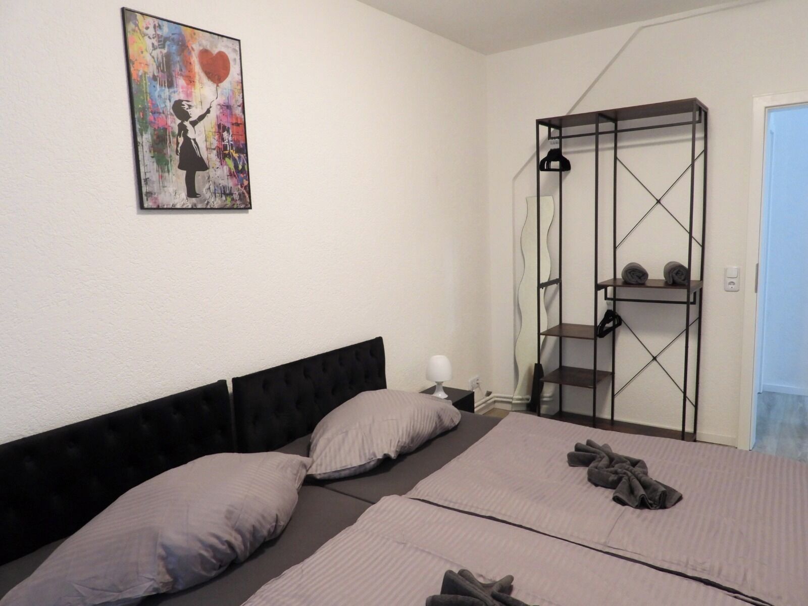 Ein Schlafzimmer mit Bett, Kissen, einem Gemälde, einem Kleiderschrank und einer Lampe.