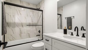 Une salle de bain moderne avec une douche à parois de verre, des toilettes blanches et un meuble-lavabo avec un évier et un miroir.