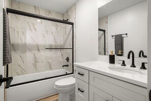 Et moderne badeværelse med en bruseniche med glasvægge, et hvidt toilet og en vaskebord med håndvask og spejl.