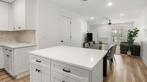 Une cuisine moderne avec des meubles blancs, un îlot central et un coin repas comprenant une table et des chaises en bois foncé.