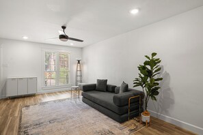 Un saló modern amb un sofà gris, una làmpada de peu, un ventilador de sostre i una planta gran.