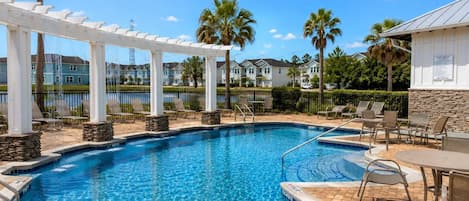 A swimming pool with a white pergola, lounge chairs, and a stone wall.