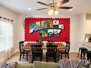 A dining area with a red wall mural, a ceiling fan, and a wooden dining table with chairs. - Beach Days and Pool Nights - PCB Sleeps 8 (Panama City Beach)
