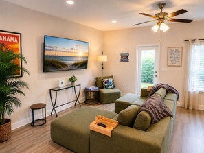 A living room with a sofa, a coffee table, a television, and a ceiling fan. - Beach Days and Pool Nights - PCB Sleeps 8 (Panama City Beach)