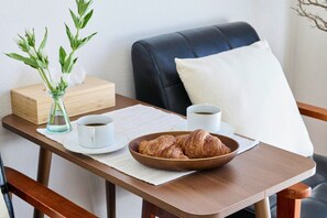 Une table dressée pour le petit-déjeuner avec des croissants, deux tasses de café, un vase rempli de fleurs et une boîte en bois.