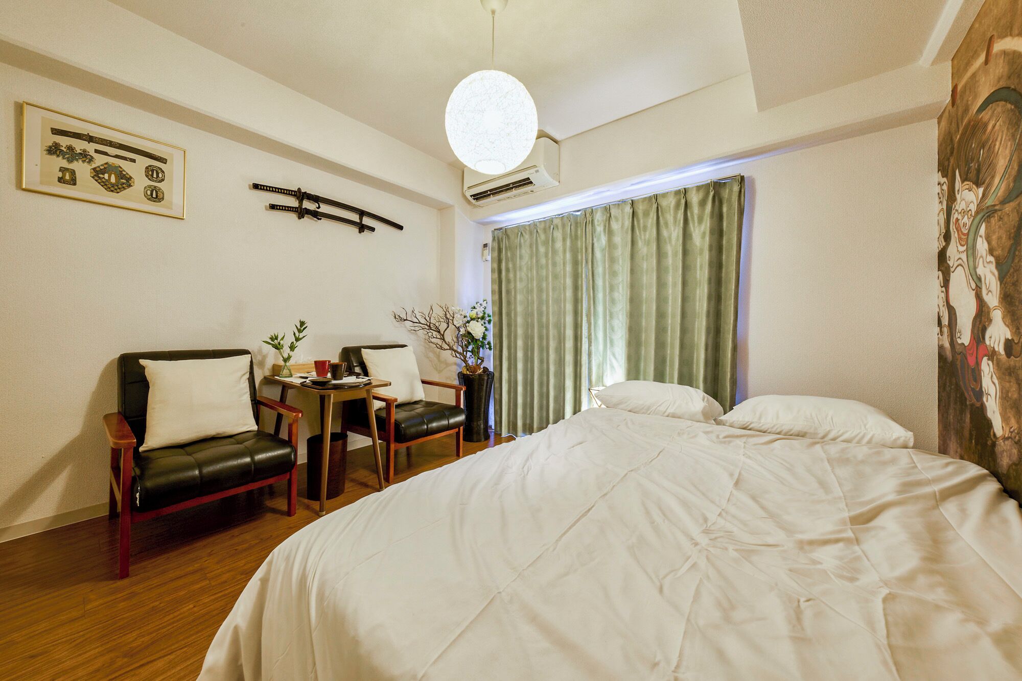 A hotel room with a bed, two chairs, a small table with a vase, and a painting on the wall.