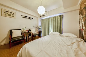 Una habitación de hotel con una cama, dos sillas, una mesita con un florero y un cuadro en la pared.