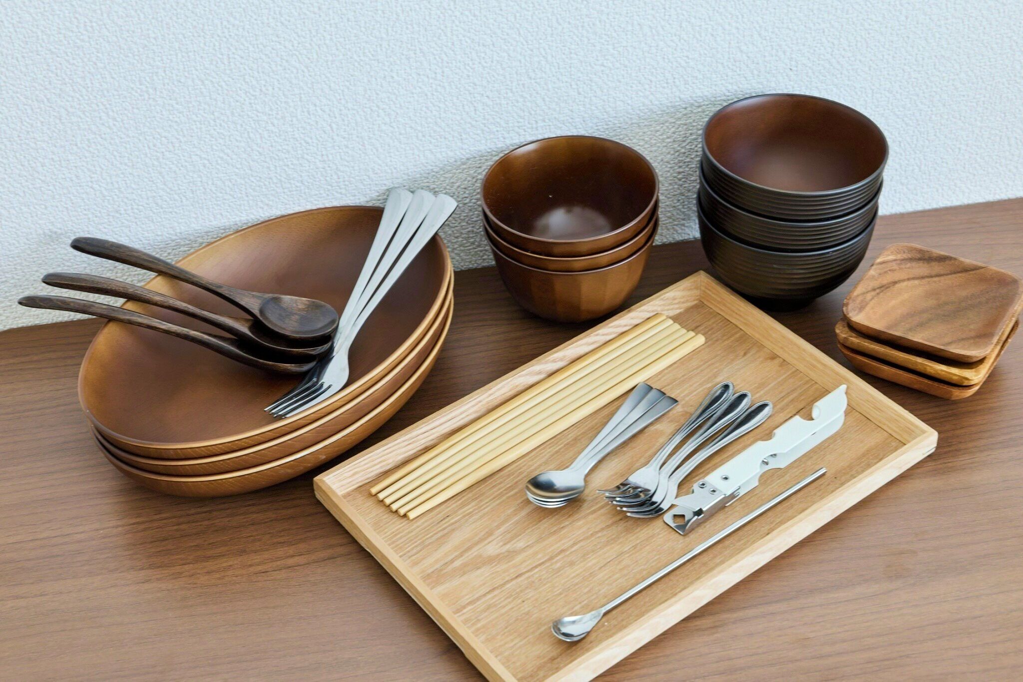 Een eettafelset met meerdere kommen, lepels, stokjes en een houten serveerplank.