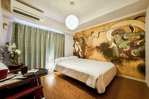 Una habitación de hotel con una cama, un mural en la pared, un escritorio con un jarrón de flores y un equipo de aire acondicionado.