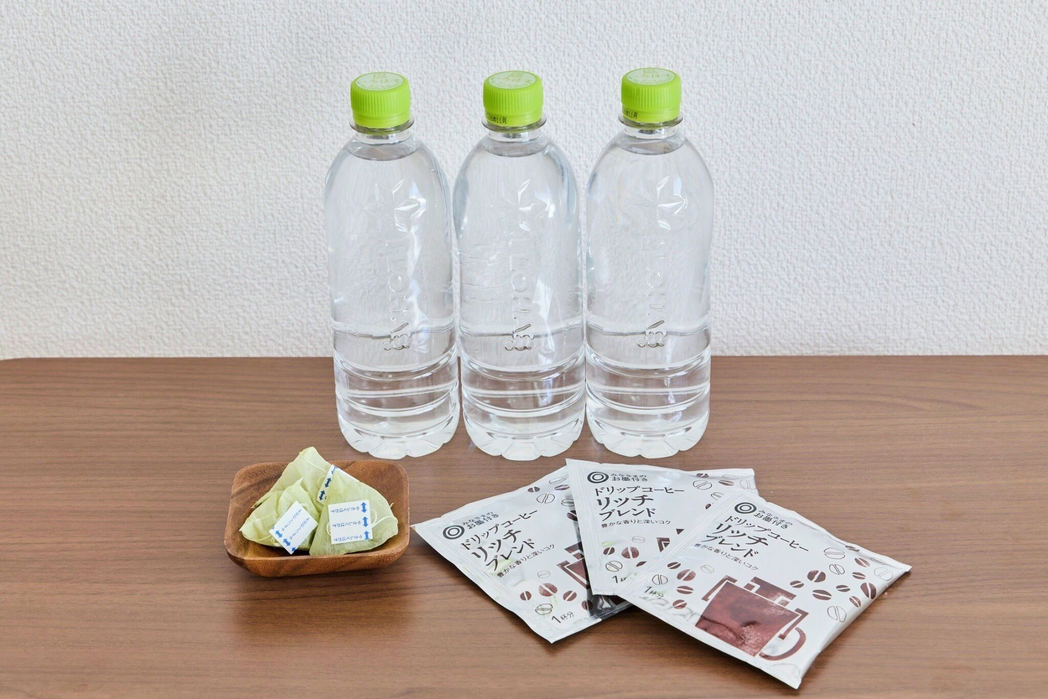 Three clear plastic bottles with green caps, a wooden tray with green tea bags, and a white wall in the background.