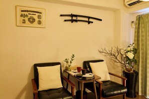 Une pièce comprenant deux fauteuils en cuir noir, une petite table avec un vase et une tasse, et un climatiseur fixé au mur.