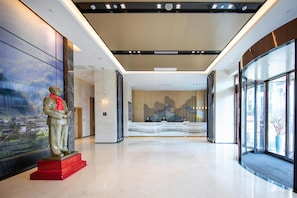 Een moderne hotel lobby met een receptiebalie, een beeld en een groot raam met uitzicht op de stad.