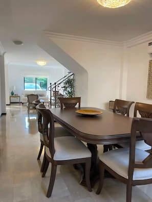 A dining area with a long table, chairs, and a chandelier.