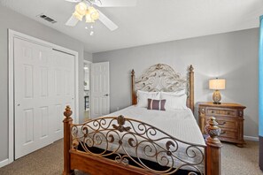 A bedroom with a large bed, a ceiling fan, a nightstand with a lamp, and a door. - Modern Retreat - Pool  - Walk to Beach (Miramar Beach)