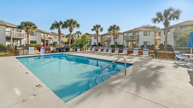 A swimming pool with lounge chairs and palm trees, surrounded by multi-story buildings. - Modern Retreat - Pool  - Walk to Beach (Miramar Beach)