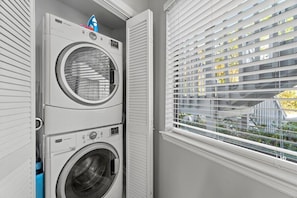 A laundry room with stacked washing machines and a window with blinds. - Modern Retreat - Pool  - Walk to Beach (Miramar Beach)