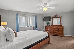 A bedroom with a bed, a dresser, a television, a ceiling fan, and a window with curtains. - Modern Retreat - Pool  - Walk to Beach (Miramar Beach)