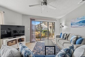 A modern living room with a flat-screen TV, a sofa set, a coffee table, and a ceiling fan. - Modern Retreat - Pool  - Walk to Beach (Miramar Beach)
