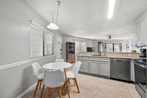 A modern kitchen with white cabinets, a dining table with chairs, and a built-in oven. - Modern Retreat - Pool  - Walk to Beach (Miramar Beach)