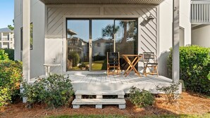 A modern house with a covered porch, a sliding glass door, and a small outdoor seating area with a table and chairs. - Modern Retreat - Pool  - Walk to Beach (Miramar Beach)