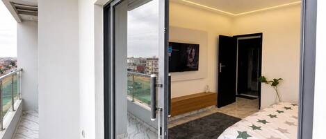 A modern bedroom with a bed, a TV, and a balcony.