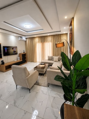 A modern living room with a sofa set, a coffee table, a TV, and a large plant. - Modern & Comfortable Residence in Angré (Abidjan)