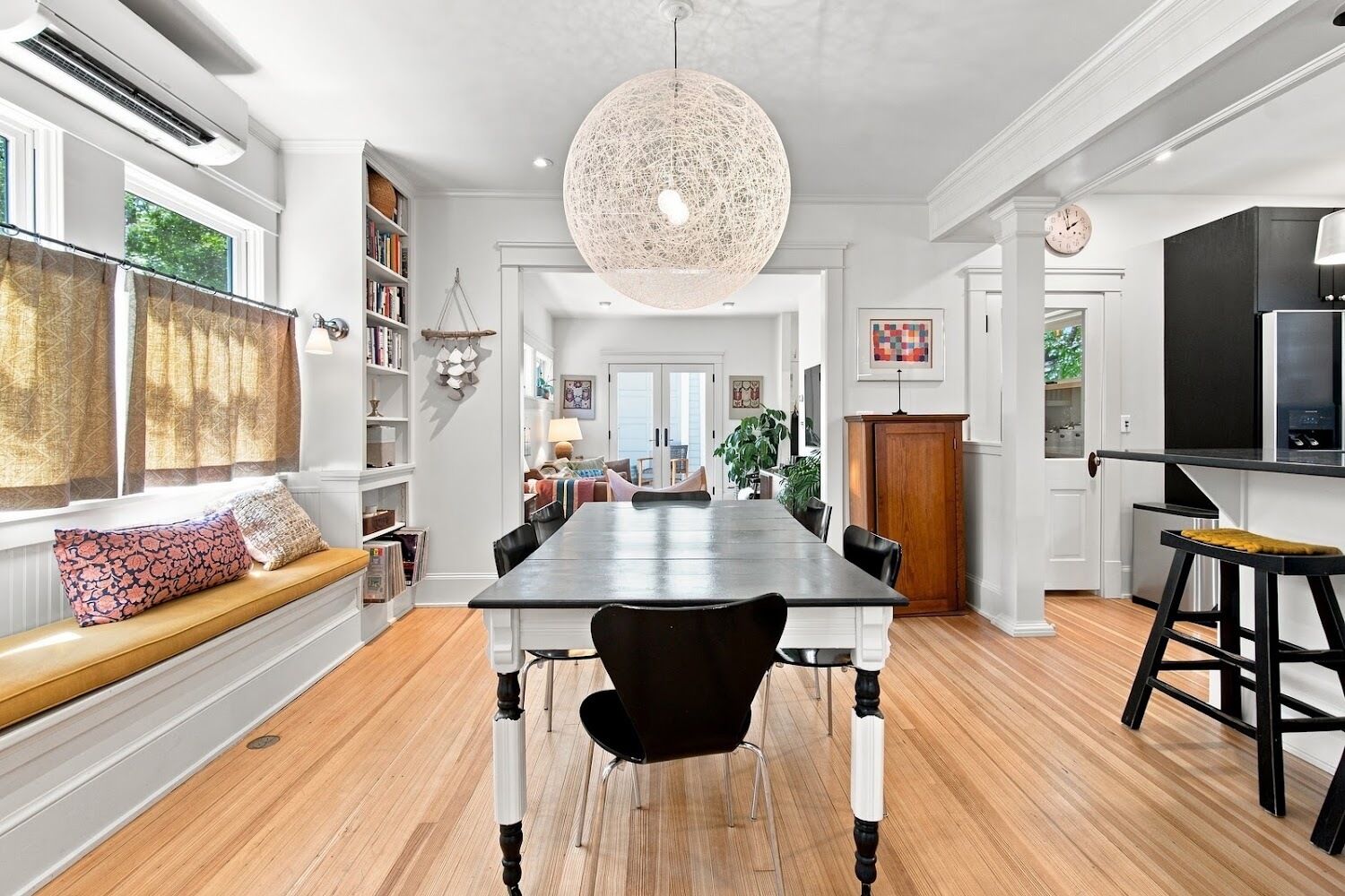 A spacious dining area with a long table, black chairs, and a large woven light fixture.