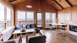A wooden interior with a dining area, sofa, and large windows offering a view of a snowy landscape. - Hlíð Cottages (Myvatn)