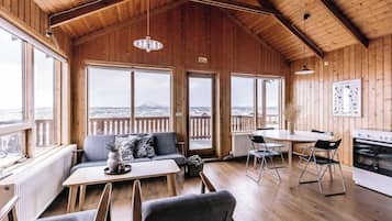 Interior de madeira com sala de jantar, sofá e janelas amplas com vista para uma paisagem nevada.