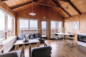 A wooden interior with a dining area, sofa, and large windows offering a view of a snowy landscape. - Hlíð Cottages (Myvatn)