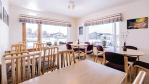 A dining area with wooden tables and chairs, large windows with curtains, and a view of the outside. - Hlíð Cottages (Myvatn)