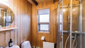 A wooden-paneled bathroom with a shower, a sink, and a window. - Hlíð Cottages (Myvatn)