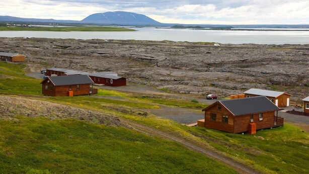 A remote cabin area with several wooden cabins, a dirt road, and a lake in the background. - Hlíð Cottages (Myvatn)