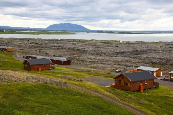 A remote cabin area with several wooden cabins, a dirt road, and a lake in the background. - Hlíð Cottages (Myvatn)