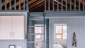 A loft-style bedroom with a wooden ceiling, a loft bed, a ladder, a window, and a bedside table. - Hlíð Cottages (Myvatn)