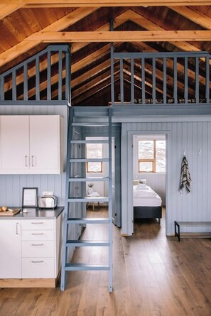 A loft-style bedroom with a wooden ceiling, a loft bed, a ladder, a window, and a bedside table. - Hlíð Cottages (Myvatn)