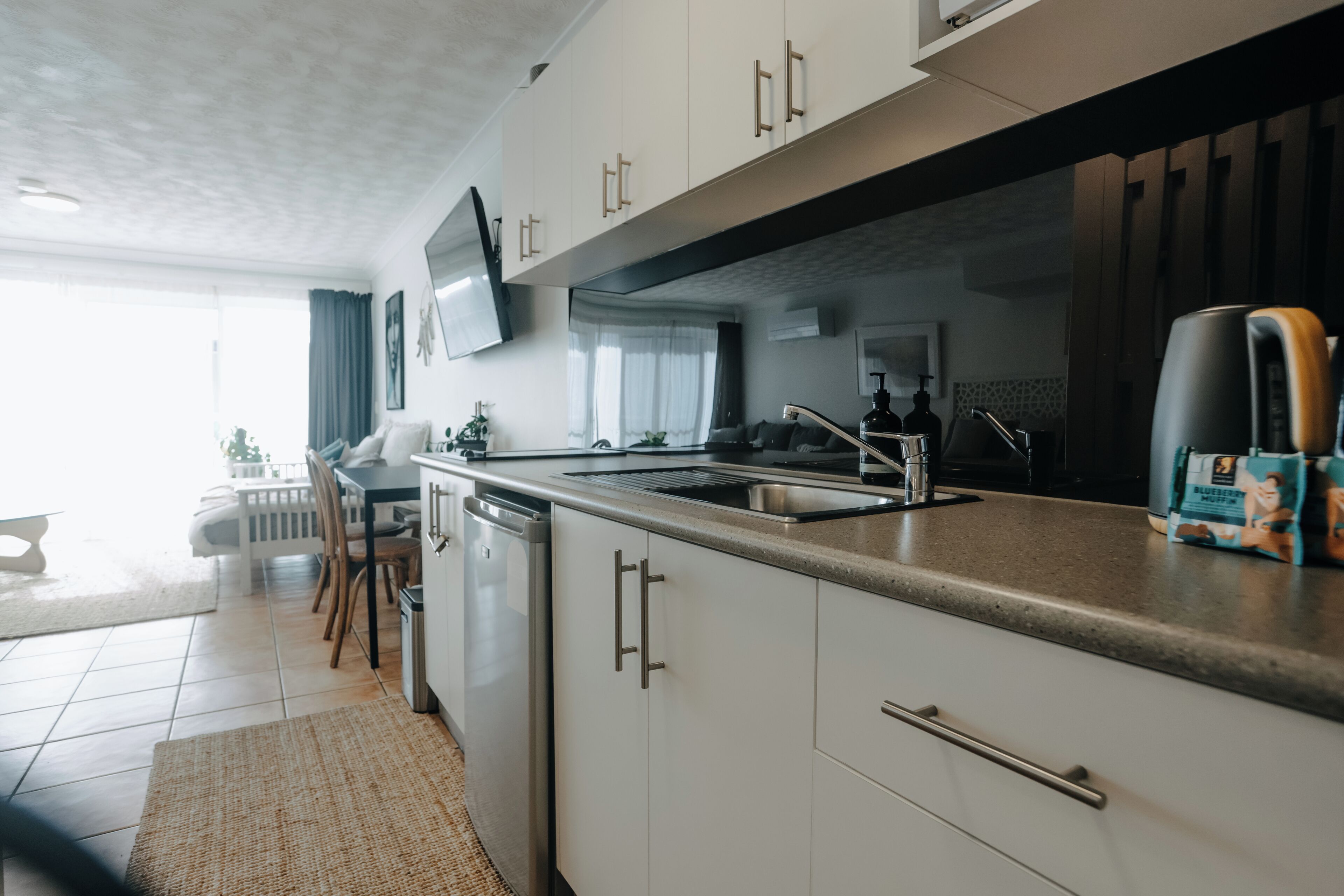 Una cocina moderna con lavavajillas integrado, un ventanal grande y un televisor de pantalla plana montado sobre la encimera.