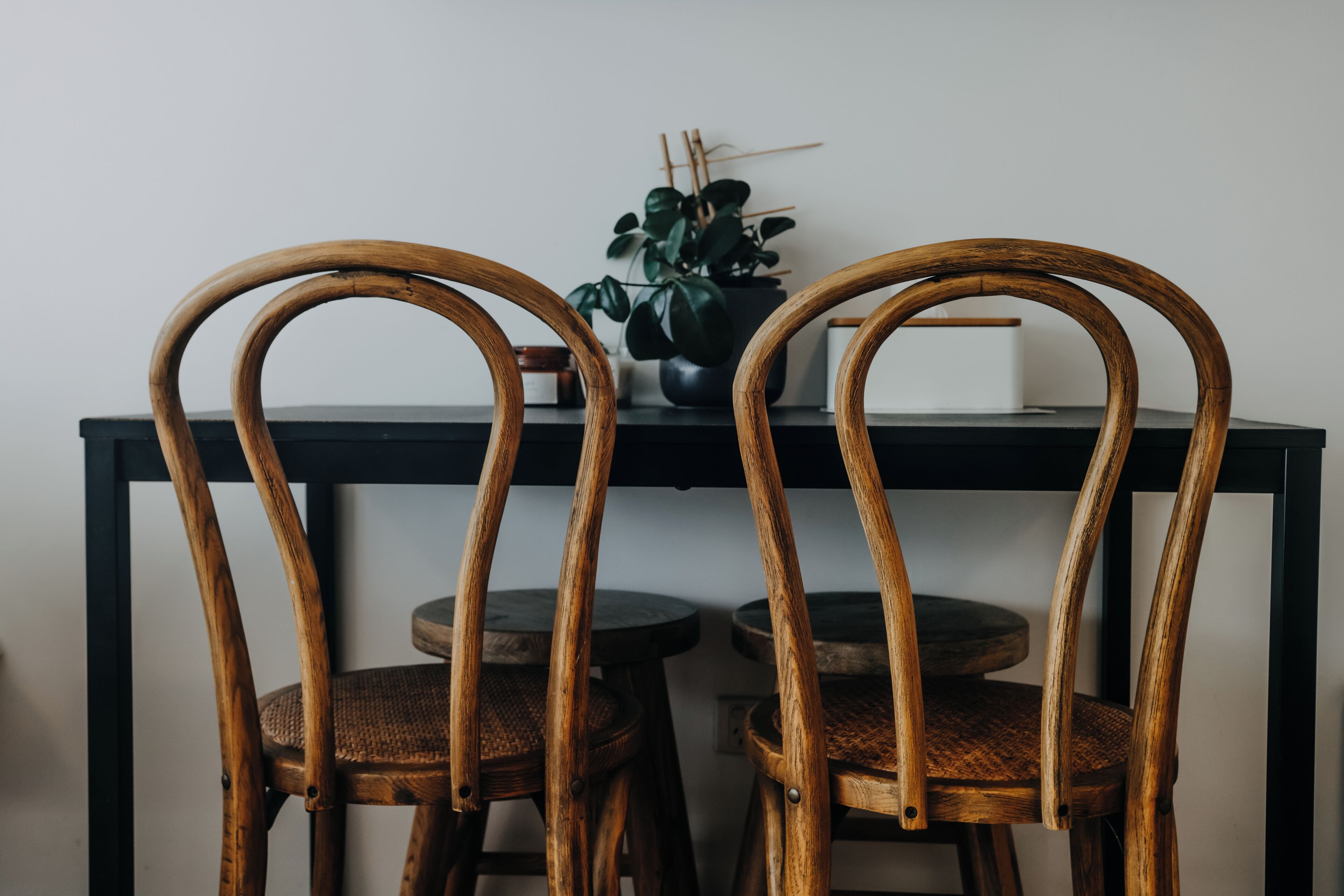 Dos sillas de madera con asientos y respaldos tejidos, ubicadas junto a una mesa con una planta en maceta.